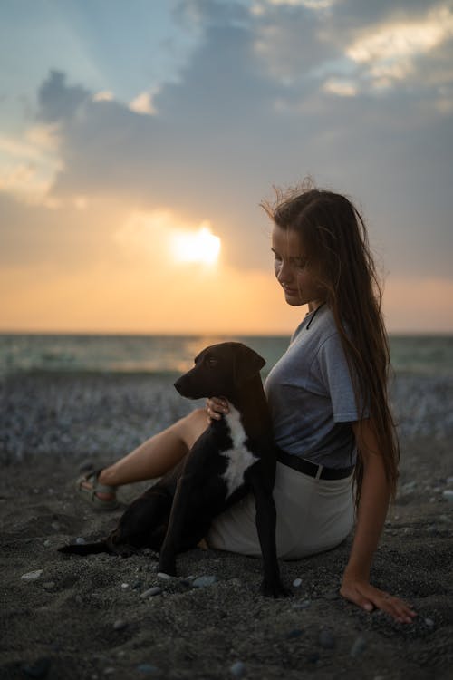A  Woman Sitting on the Shore With a Dog 