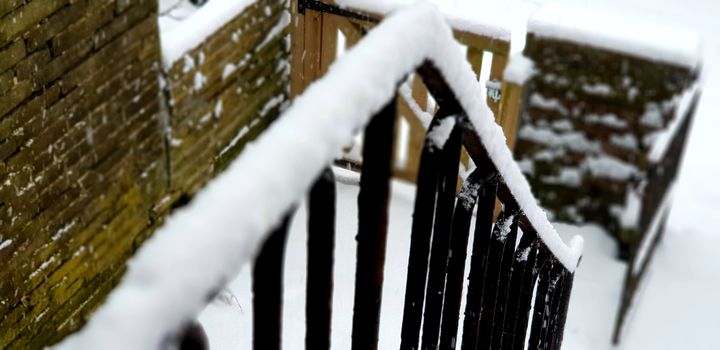 A close-up view of a snow-covered railing and brick wall outdoors in winter.