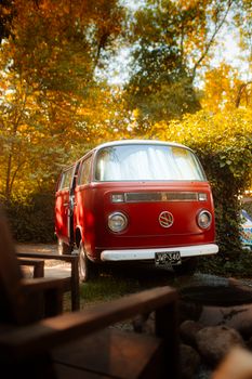 A classic red van parked amidst autumn foliage, showcasing vibrant fall colors.
