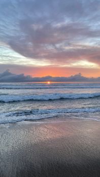 Peaceful beach at sunset with colorful sky and gentle waves rolling onto the shore.