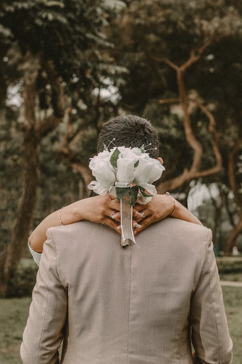 Woman Holding a White Bouquet of Flowers While Hugging a Man