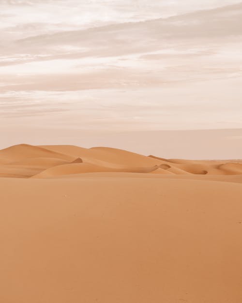 Photo of a Desert with Brown Sand Under a Cloudy Sky