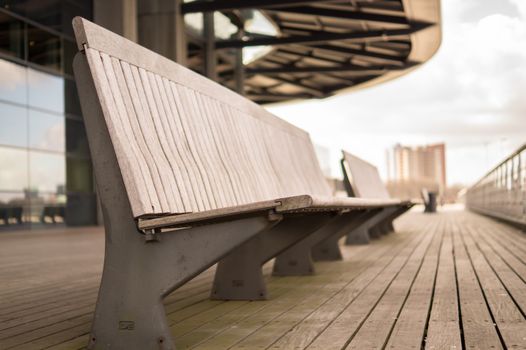 Perspective view of an empty wooden bench in a cityscape with modern architecture.
