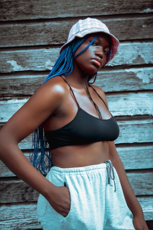 Free Young woman posing confidently in athletic wear with blue braided hair and a bucket hat. Stock Photo