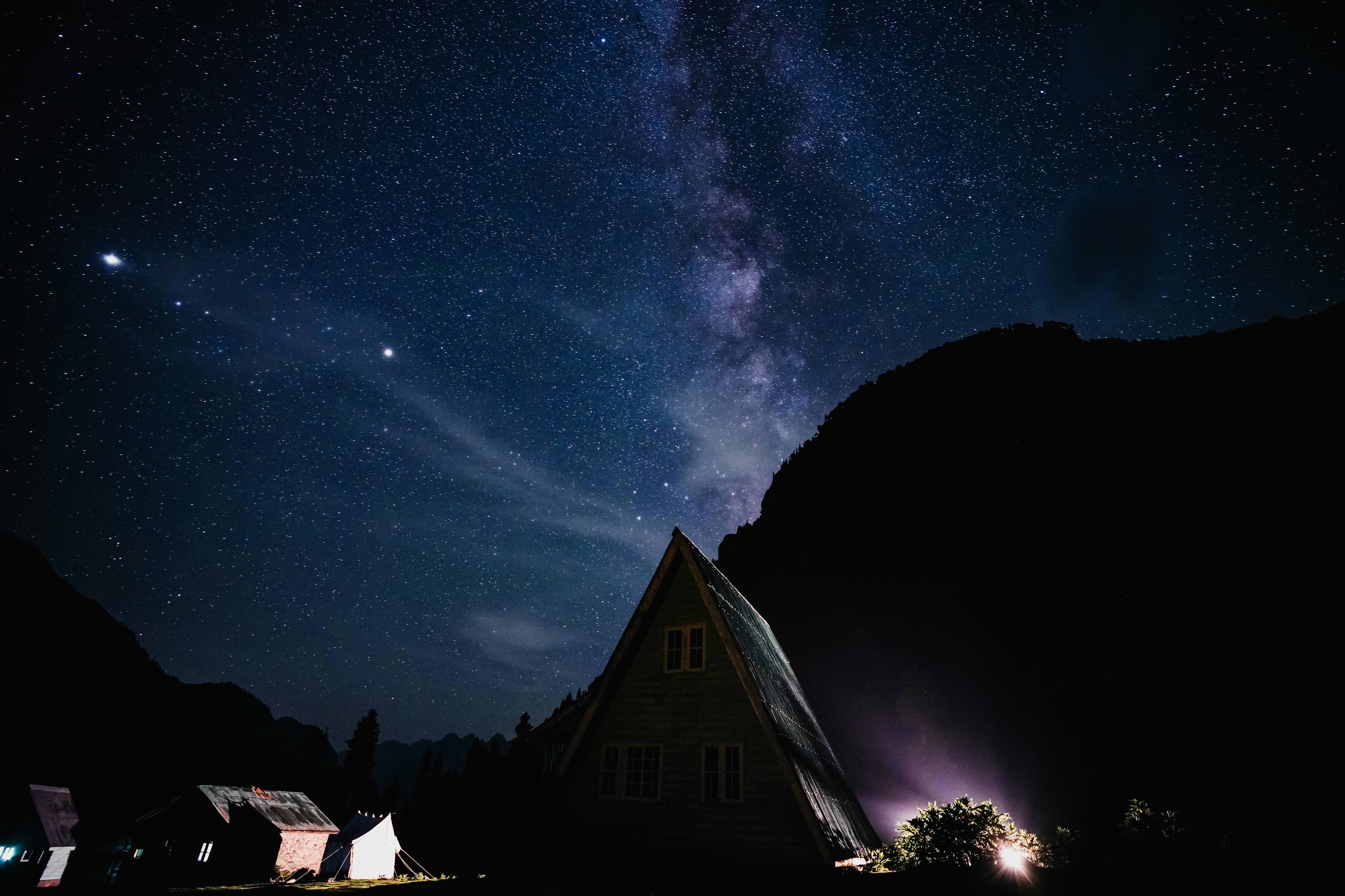 A picturesque A-frame cabin bathed in starlight with the Milky Way overhead.