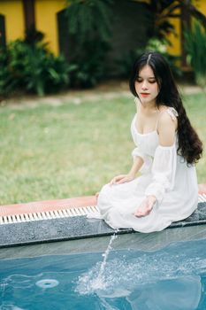 A serene moment as a woman in a white dress sits poised poolside, adding elegance to the tranquil scene.