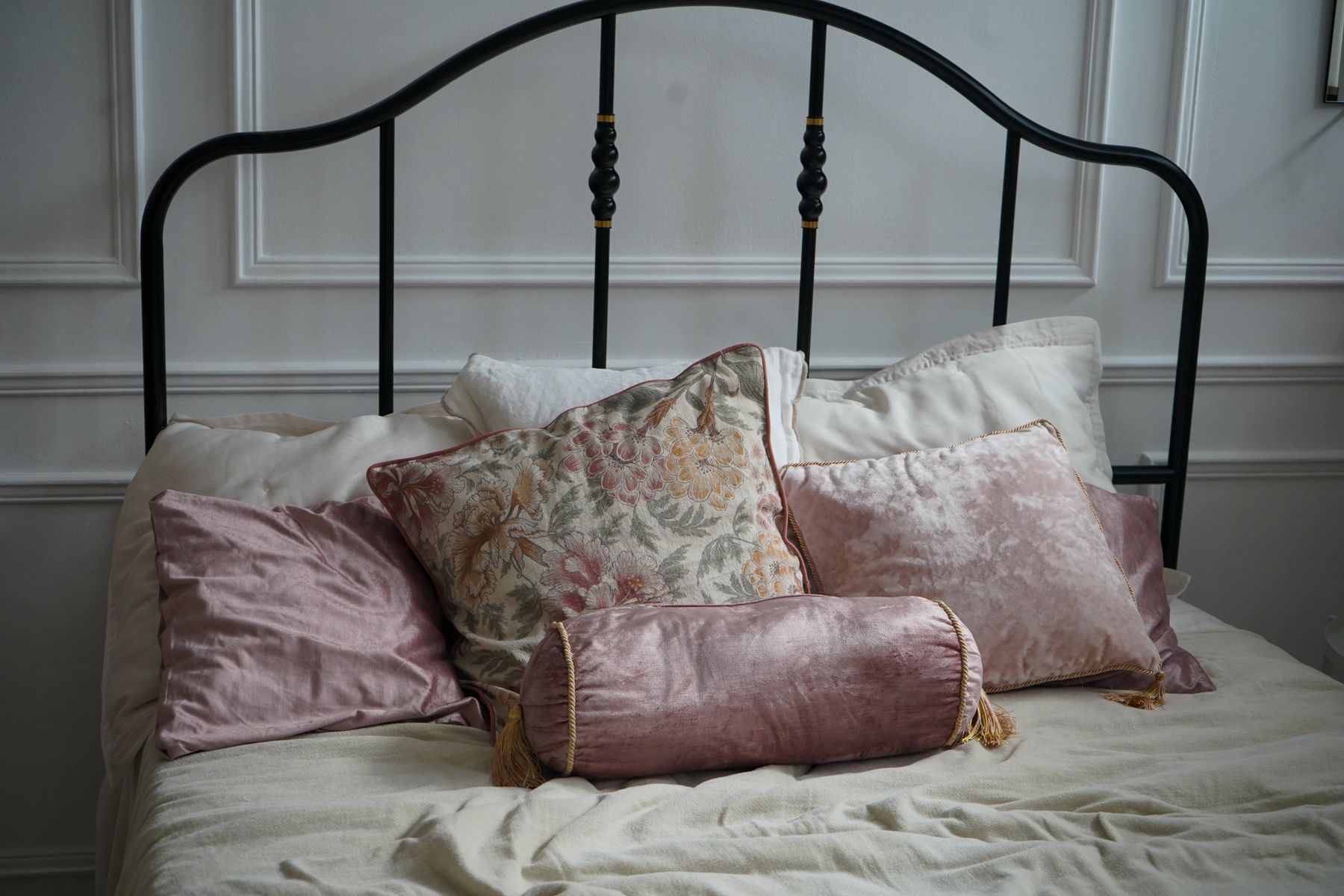 Iron bed dressed with pale linen and floral cushions in a softly colored bedroom