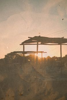 A serene beach sunset with silhouetted structures and warm tones.