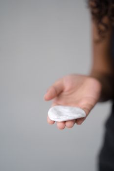 A close-up of a hand holding a soft cotton pad on a neutral background.
