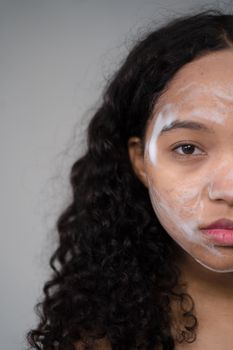 Close-up of a woman with curly hair applying a facial mask, promoting skincare routine.