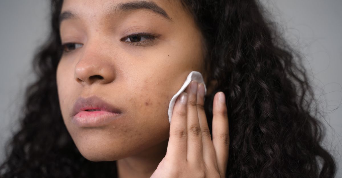 Close-up of a black woman gently applying skincare product on her face, focusing on clear and healthy skin.