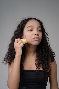 A young woman applies skincare product to her face, focusing on self-care routines.