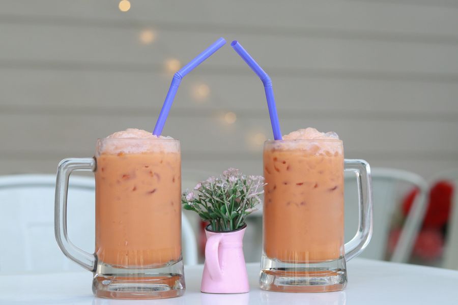 Two glasses of iced milk tea with straws beside a small flower vase — Taithong SISAYKEO on Pexels