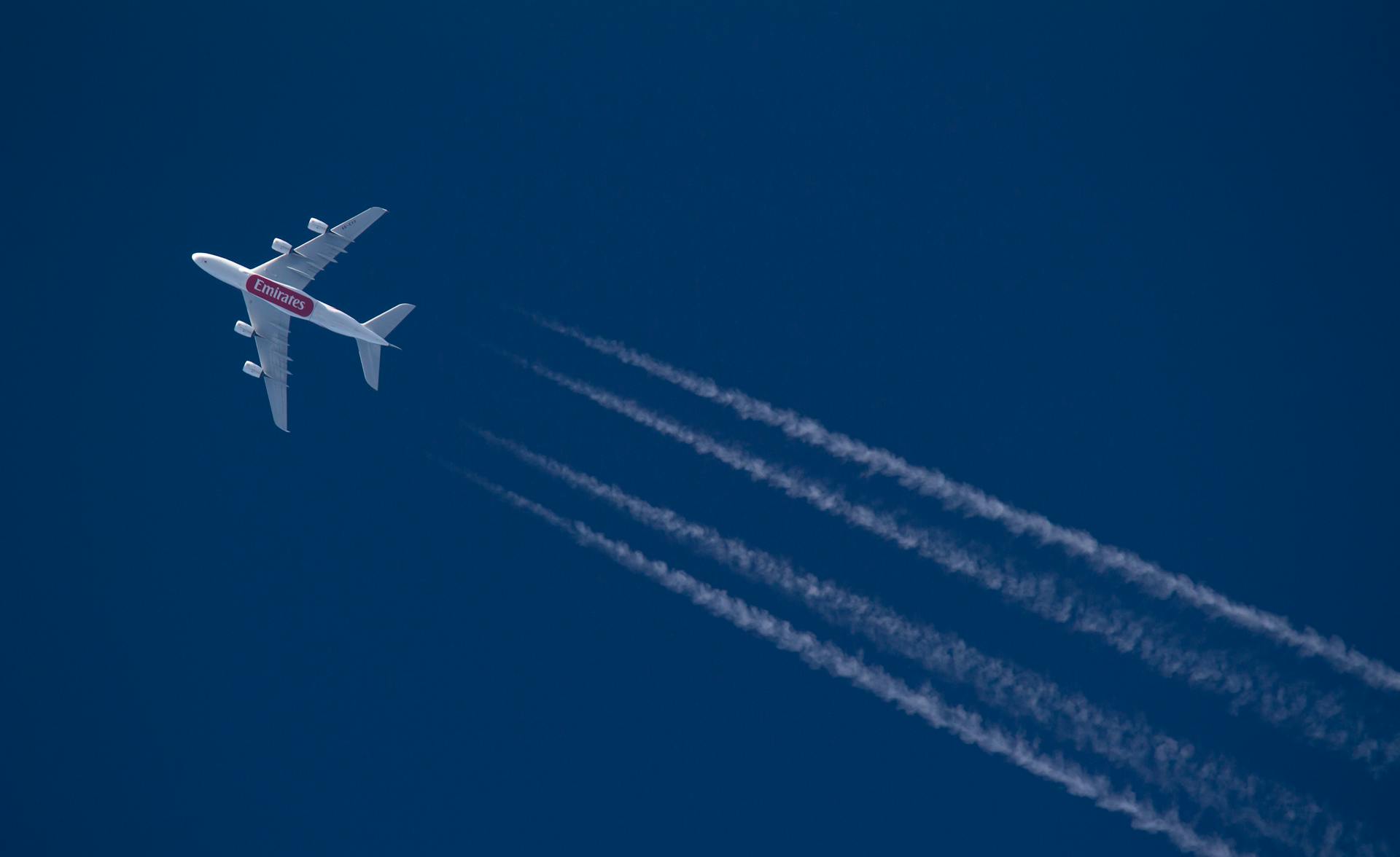 A commercial airliner cruising in a clear blue sky leaving contrails behind.