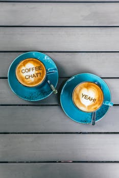 Overhead view of latte art in blue cups on a wooden table, inviting a coffee chat.