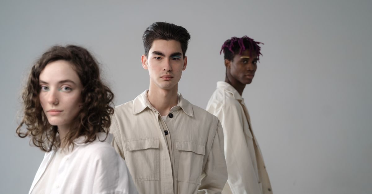 Group of diverse multiethnic young people wearing light beige and white cotton clothes standing in studio and looking at camera on gray background