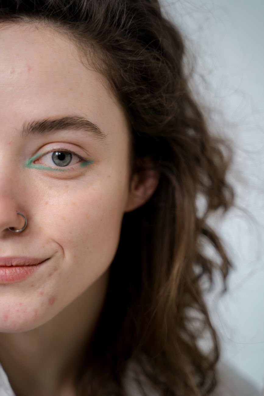 Artistic close-up portrait featuring a young woman with a nose ring and wavy hair.
