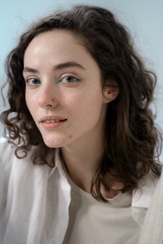 Close-up portrait of a young woman with curly hair and natural makeup, wearing a nose ring.