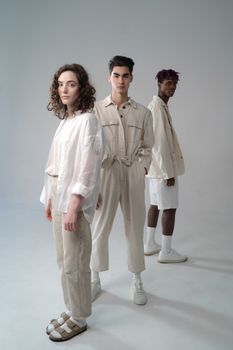 A diverse group of three young adults standing in a minimalist studio setting. Neutral tones.
