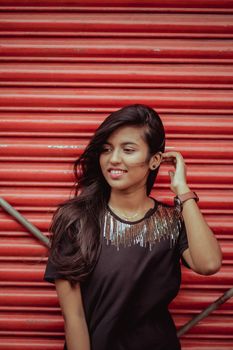 A fashionable young woman with long hair poses confidently in front of a vibrant red shutter.