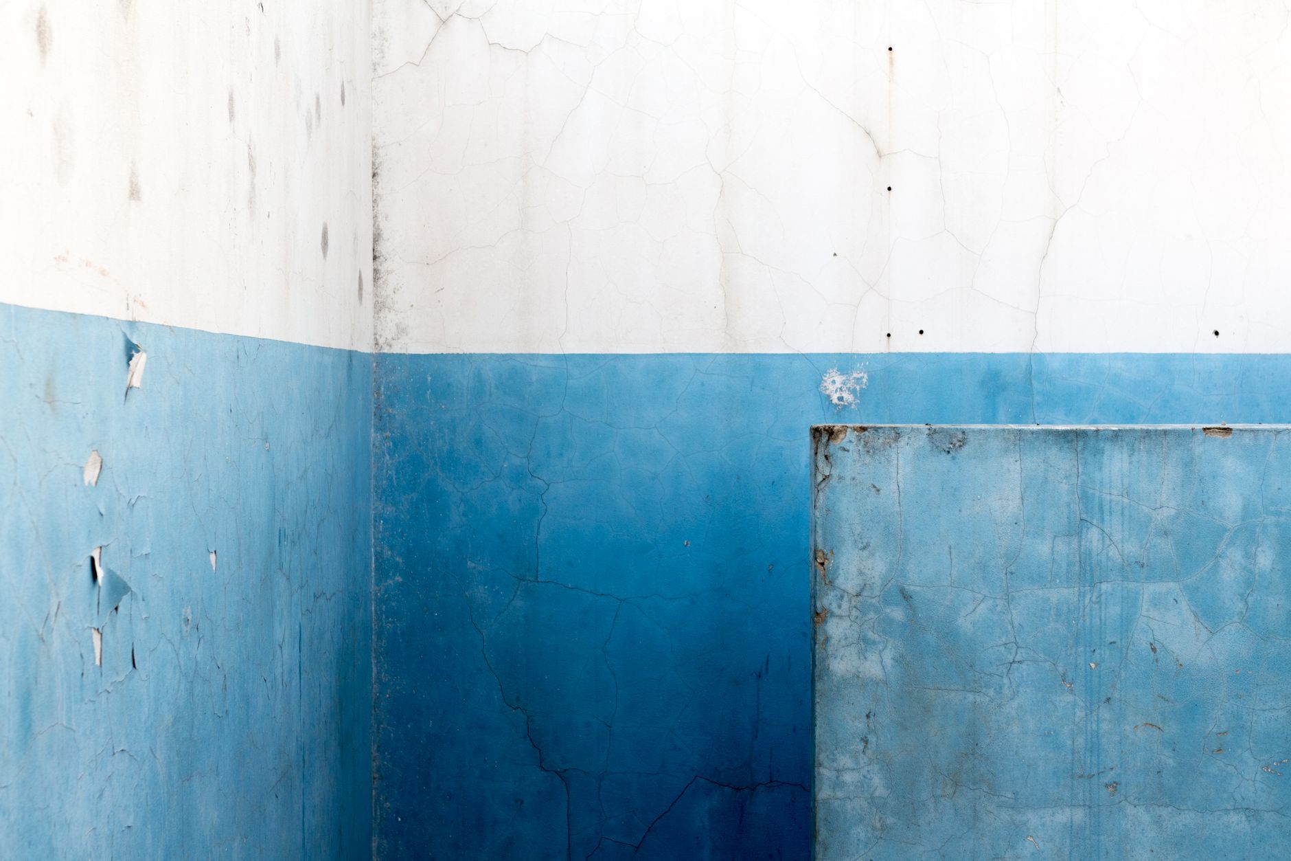 A detailed abstract view of a worn blue wall with cracked paint.
