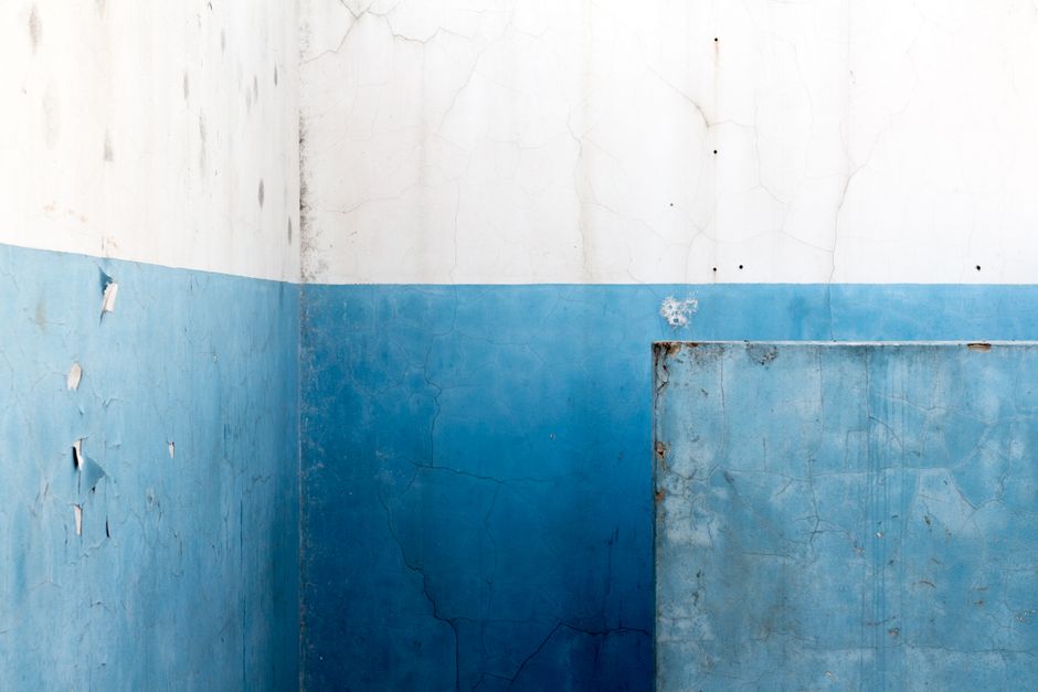 A detailed abstract view of a worn blue wall with cracked paint.
