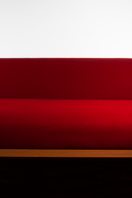 A modern red couch with wooden trim against a minimalist white wall, emphasizing clean lines and vibrant color contrast.