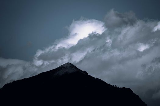 Moody silhouette of a mountain with dramatic clouds in the evening sky.