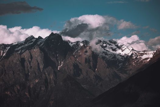 Dramatic view of rugged snow-capped mountains with cloudy sky.