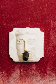 方形大理石喷泉雕塑映衬着充满活力的红色墙壁，描绘了一张脸