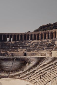 Photo of a grand ancient Roman amphitheater with stone arches on a sunny day.