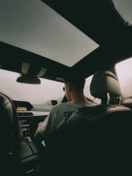 Back seat view of two people driving in a car on a cloudy day.