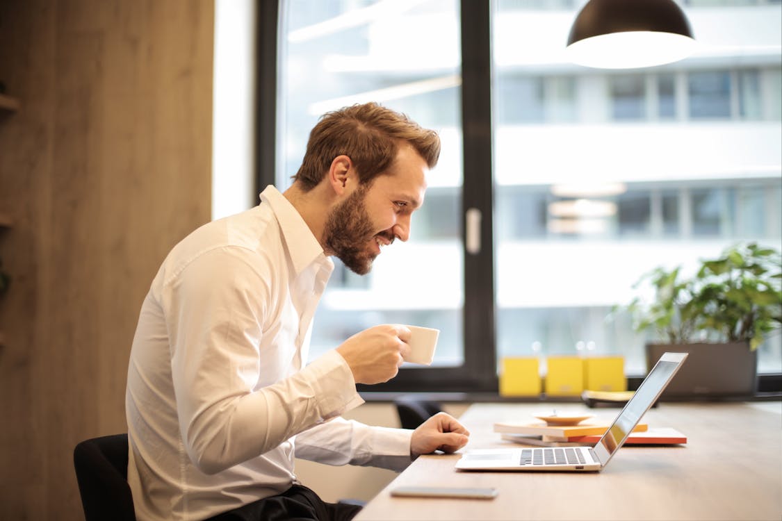 Free Man Holding Teacup Infront of Laptop on Top of Table Inside the Room Stock Photo