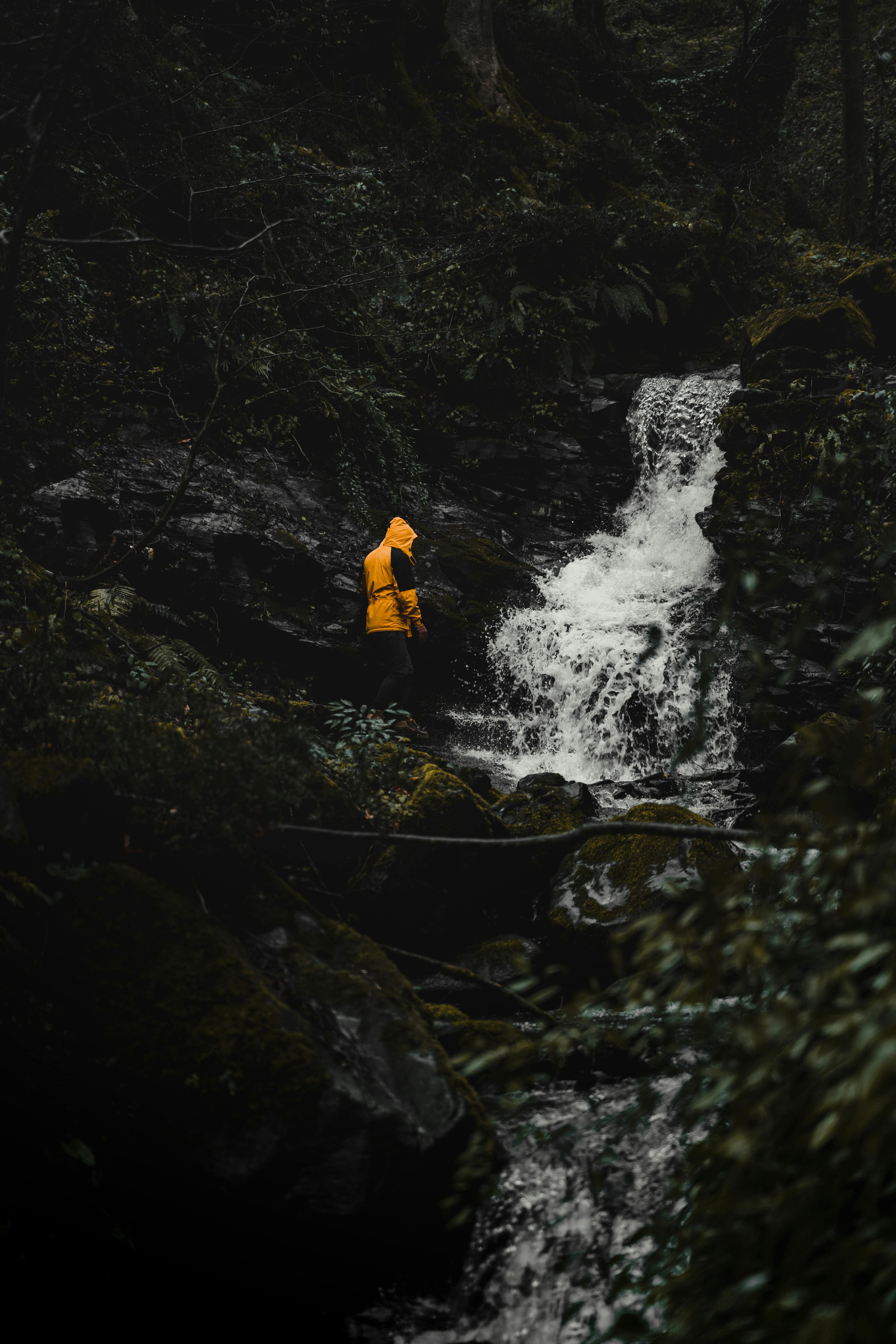 Waterproof shell jacket on a forest trail near a stream, ideal for wind and rain protection.