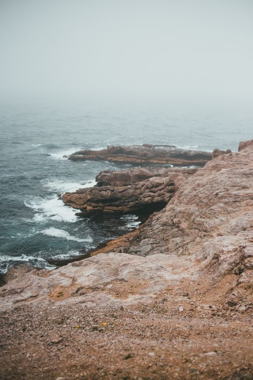 Free A serene rocky coastline under foggy and overcast conditions, capturing the natural landscape. Stock Photo