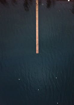 这张自上而下的照片中，长长的木码头延伸至平静的深蓝色湖泊，呈现出一派宁静的景观