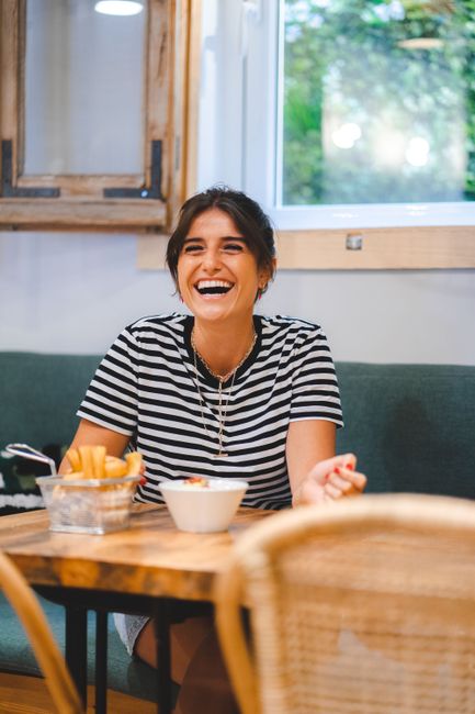 Smiling woman in striped shirt dining inside a cozy restaurant setting.