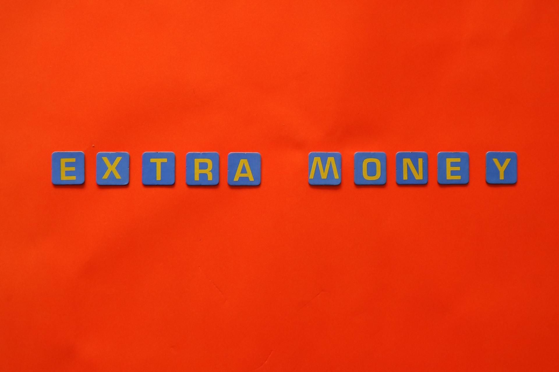 Bright orange background with 'EXTRA MONEY' spelled in blue and yellow tiles, illustrating financial concepts.