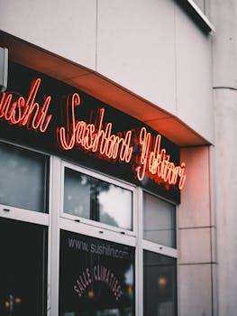 Close-up view of a neon sign reading sushi, sashimi, yakitori outside a restaurant with a glass door.