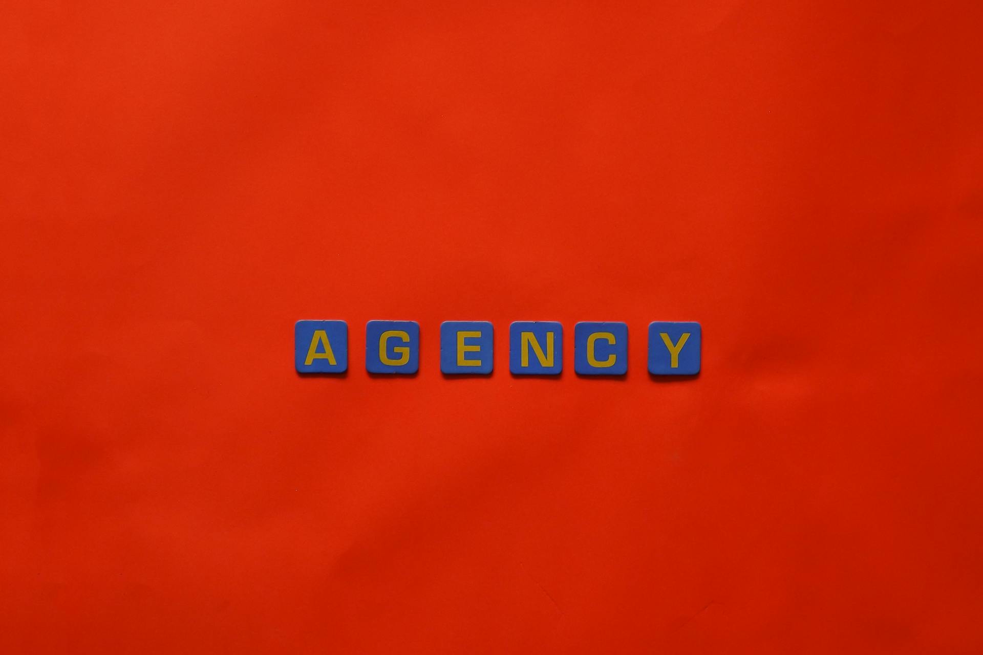 Blue letter tiles spelling 'AGENCY' on a vibrant red background, ideal for creative promotion.