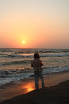 A person stands on the beach watching a beautiful sunset over the ocean waves.