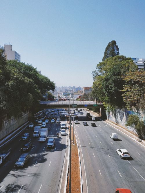 Free Aerial view of a bustling urban highway with cars and lush greenery on a sunny day. Stock Photo