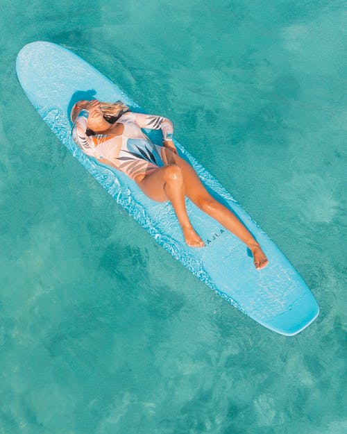 High Angle View of a Tanned Woman Floating on a Blue Surfboard in a Turquoise Sea