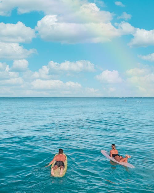 Woman and Man on Surfboards under Rainbow