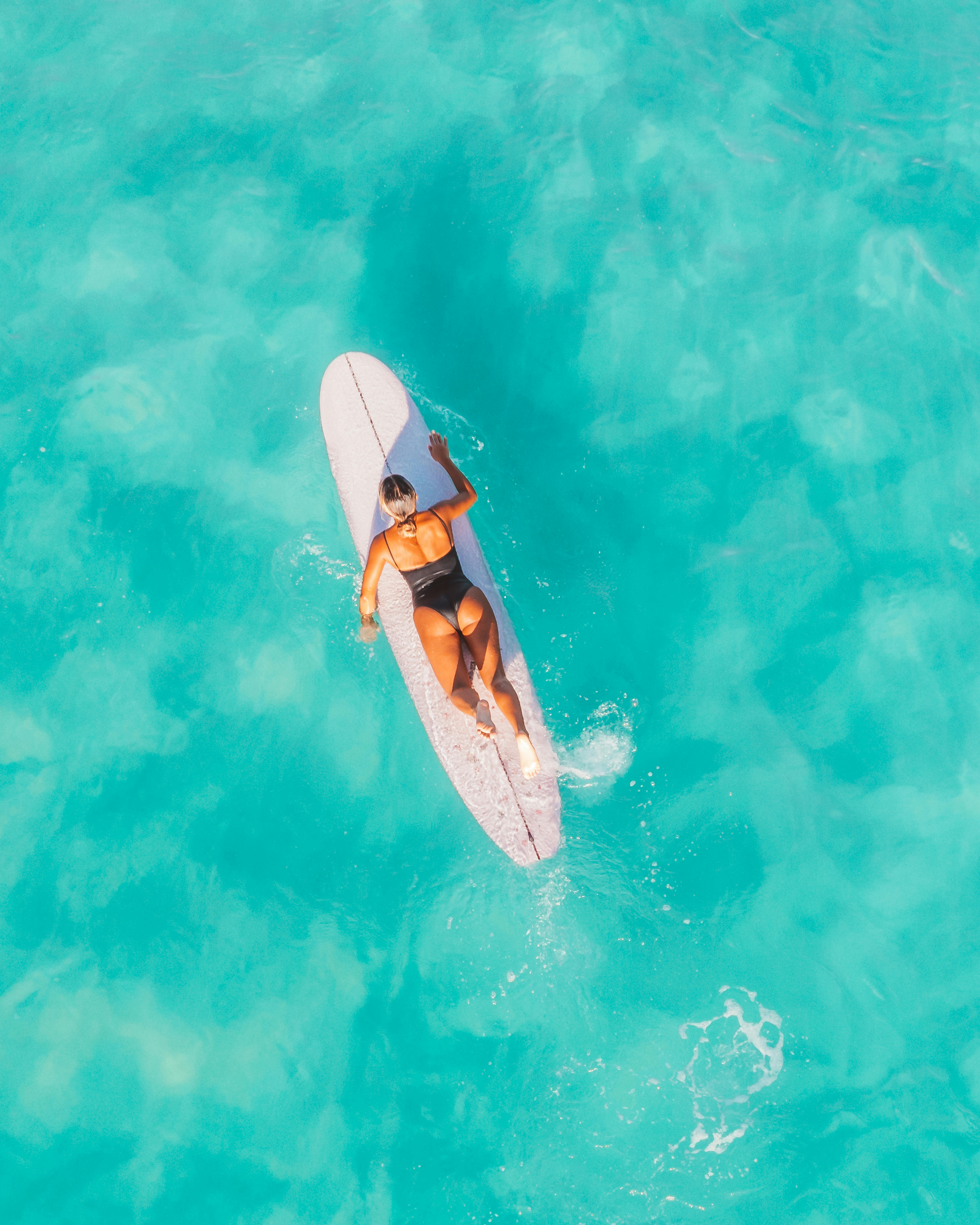 Aerial shot of a woman on a surfboard in clear turquoise water, enjoying summer vibes.