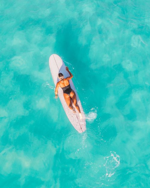 Free Aerial shot of a woman on a surfboard in clear turquoise water, enjoying summer vibes. Stock Photo