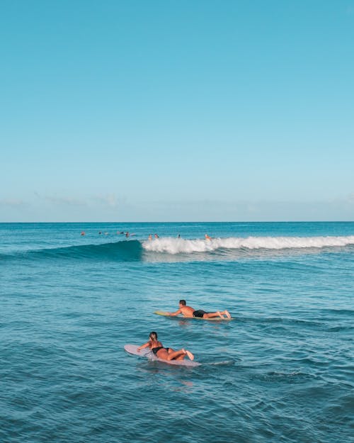 A Man and a Woman Lying on Surfboards on a Blue Beach