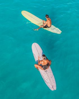 Two surfers resting on their boards in a clear turquoise sea, offering a peaceful and vibrant scene.