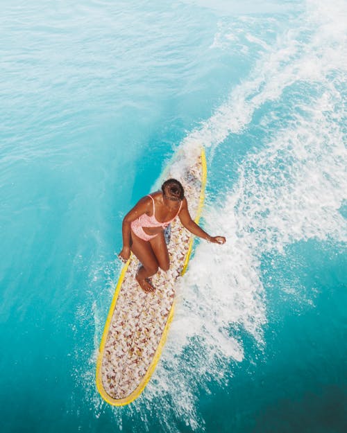Woman in Pink Swimwear Standing on White Surfboard on Body of Water