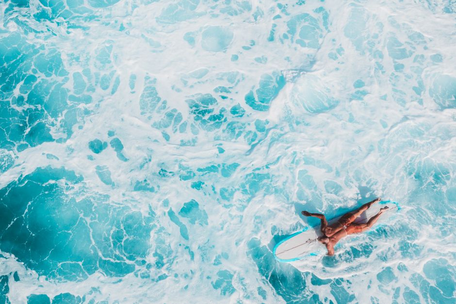 A surfer paddling through vibrant turquoise ocean waves viewed from above. Perfect for beach and surf lifestyle themes.